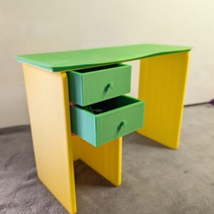 Modern 3D printed miniature dollhouse desk with a green top, yellow legs, and two functional green drawers pulled slightly open.