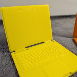 Modern 3D printed miniature laptops for dollhouses in yellow and orange with functional folding screens and detailed keyboards.