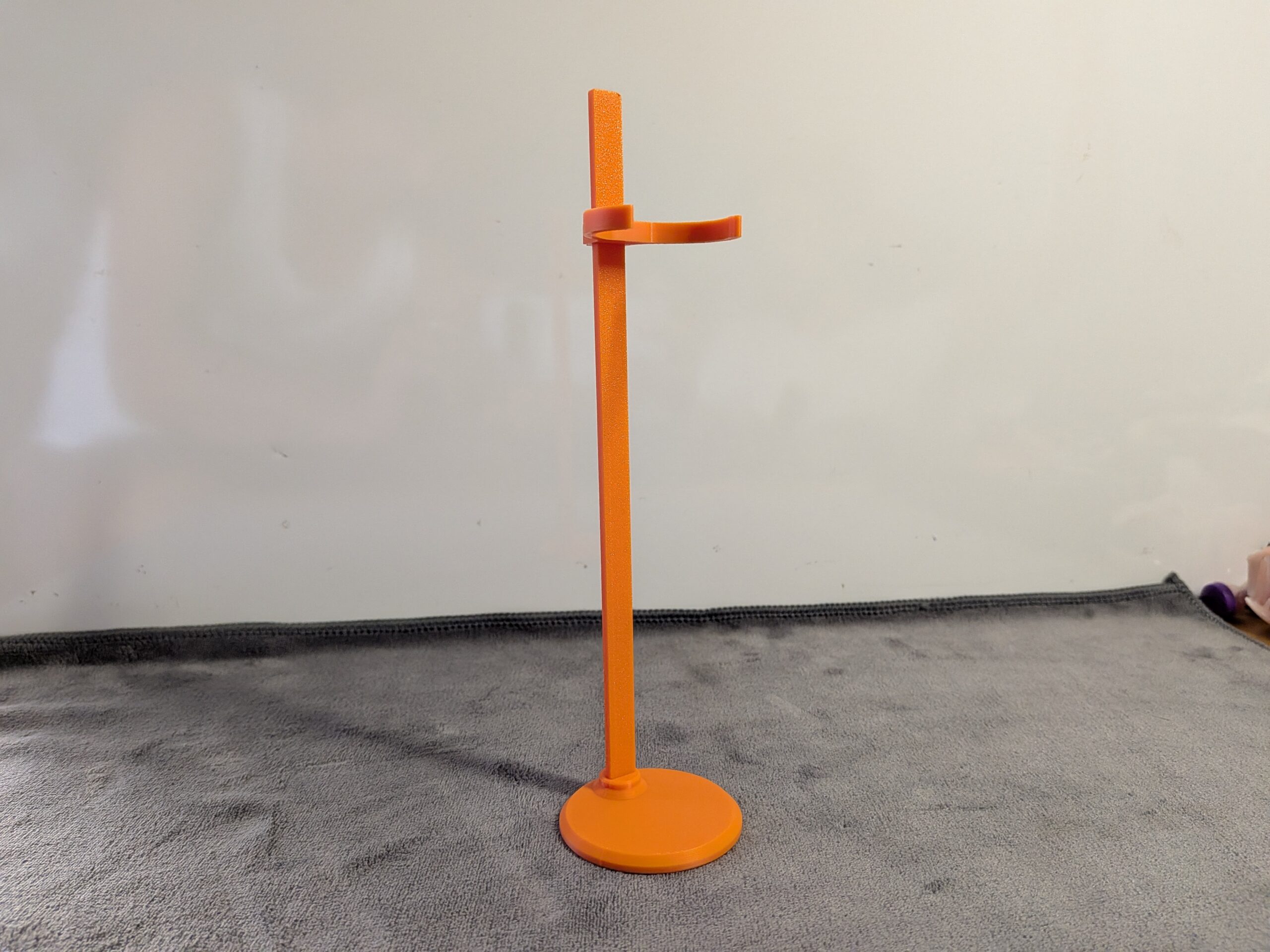 Vibrant orange 3D printed doll display stand featuring a round base and adjustable waist clip, shown supporting a fashion doll.